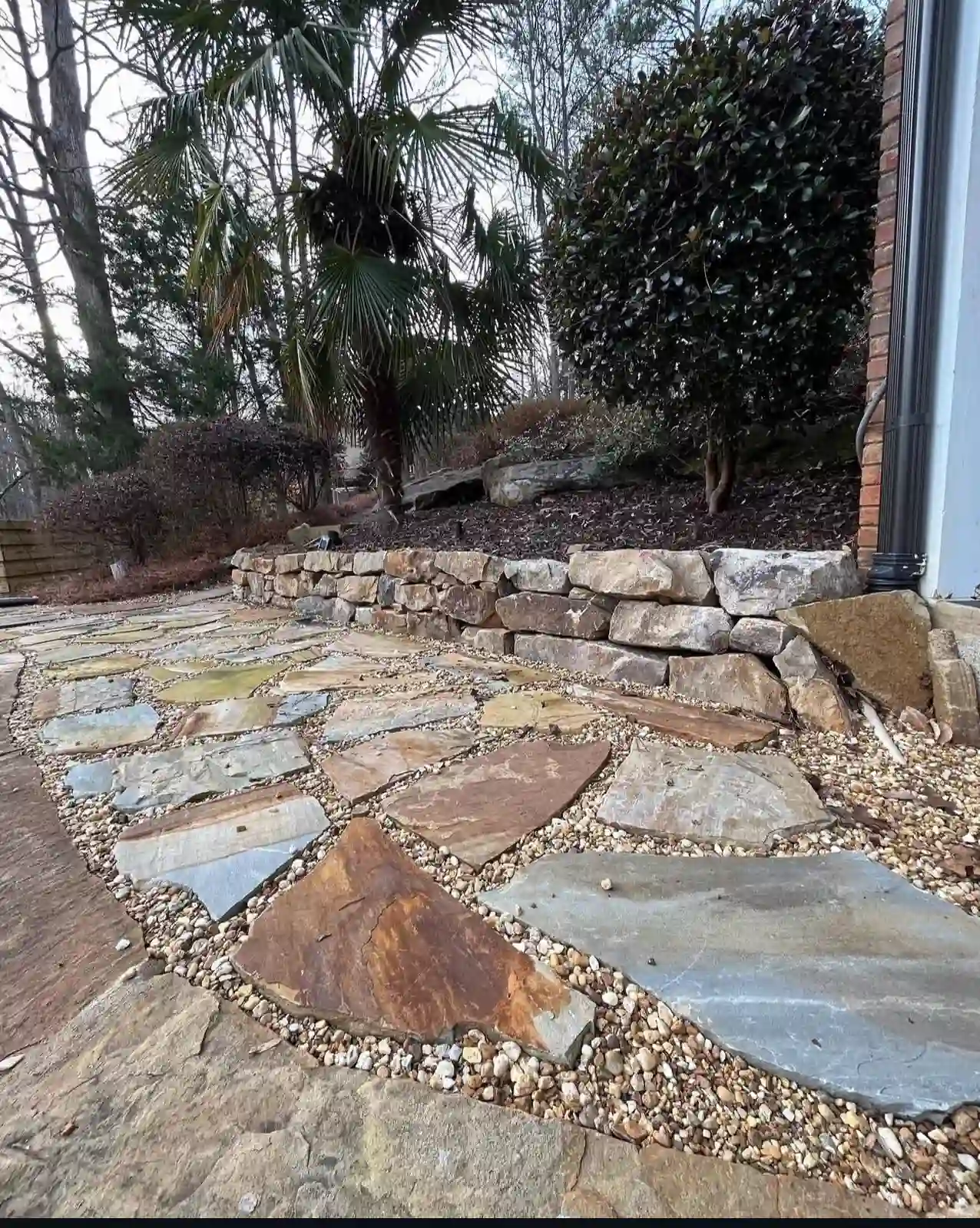 Flagstone patio installation with stacked stone retaining wall in Alpharetta, GA